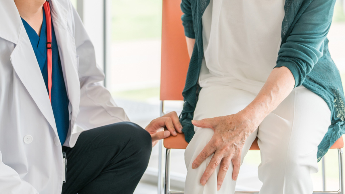 膝を押さえる高齢女性と寄り添う医師